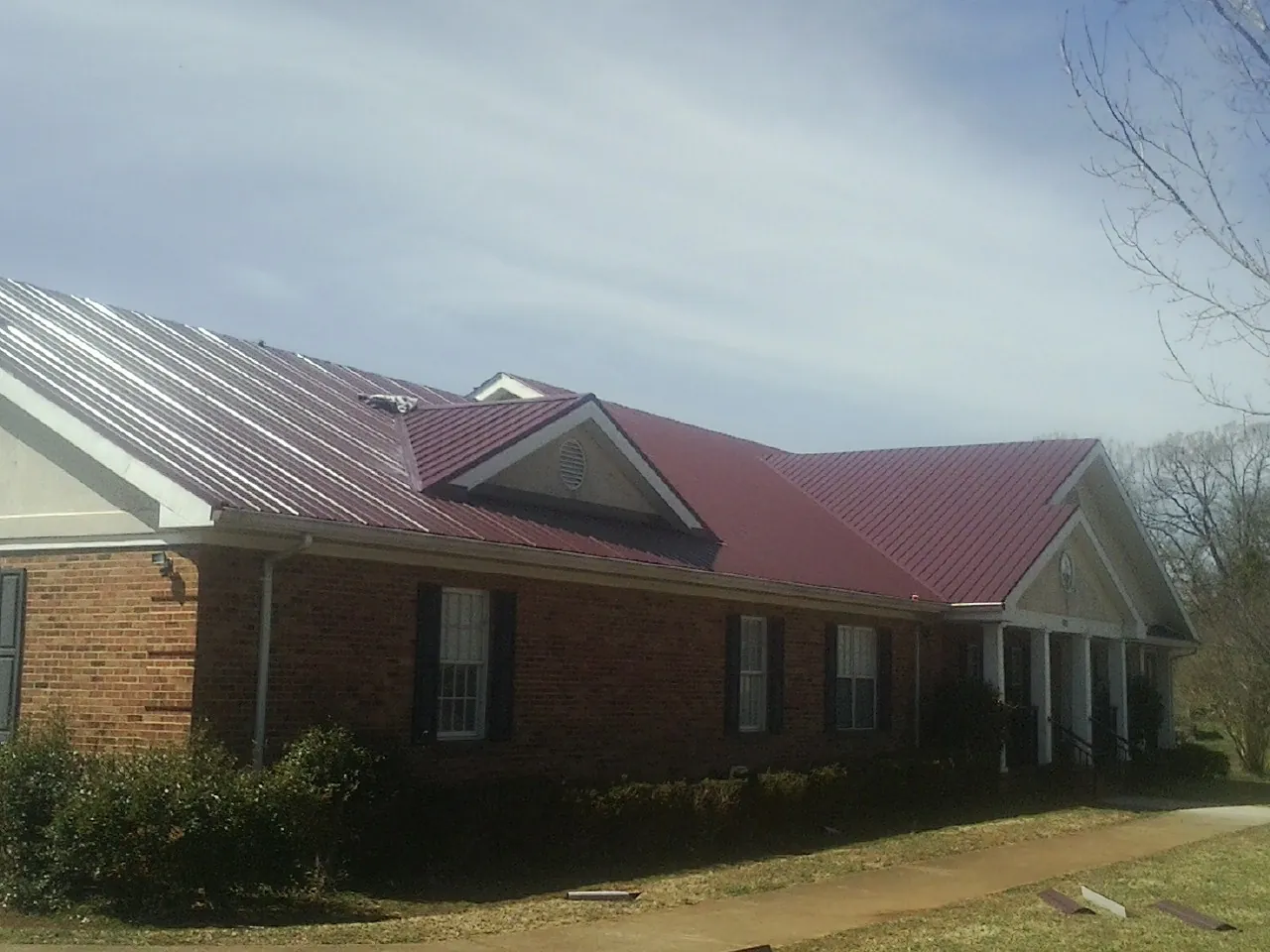 Red metal roof with gabled entries on a long brick building, from a Hail Damage Roof Repair job in Crab Orchard