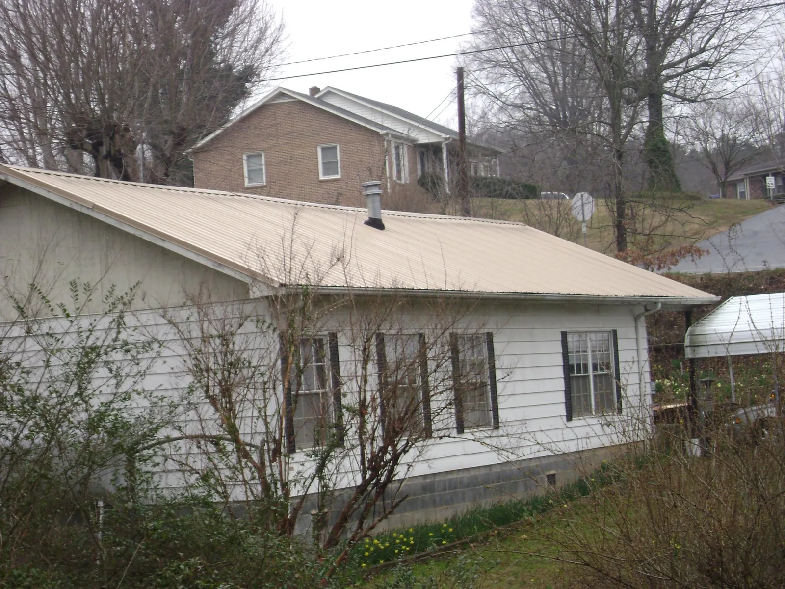 Tan metal roof on a white sided house set into a hillside — Commercial Roofing by Roofing Brothers in Crab Orchard