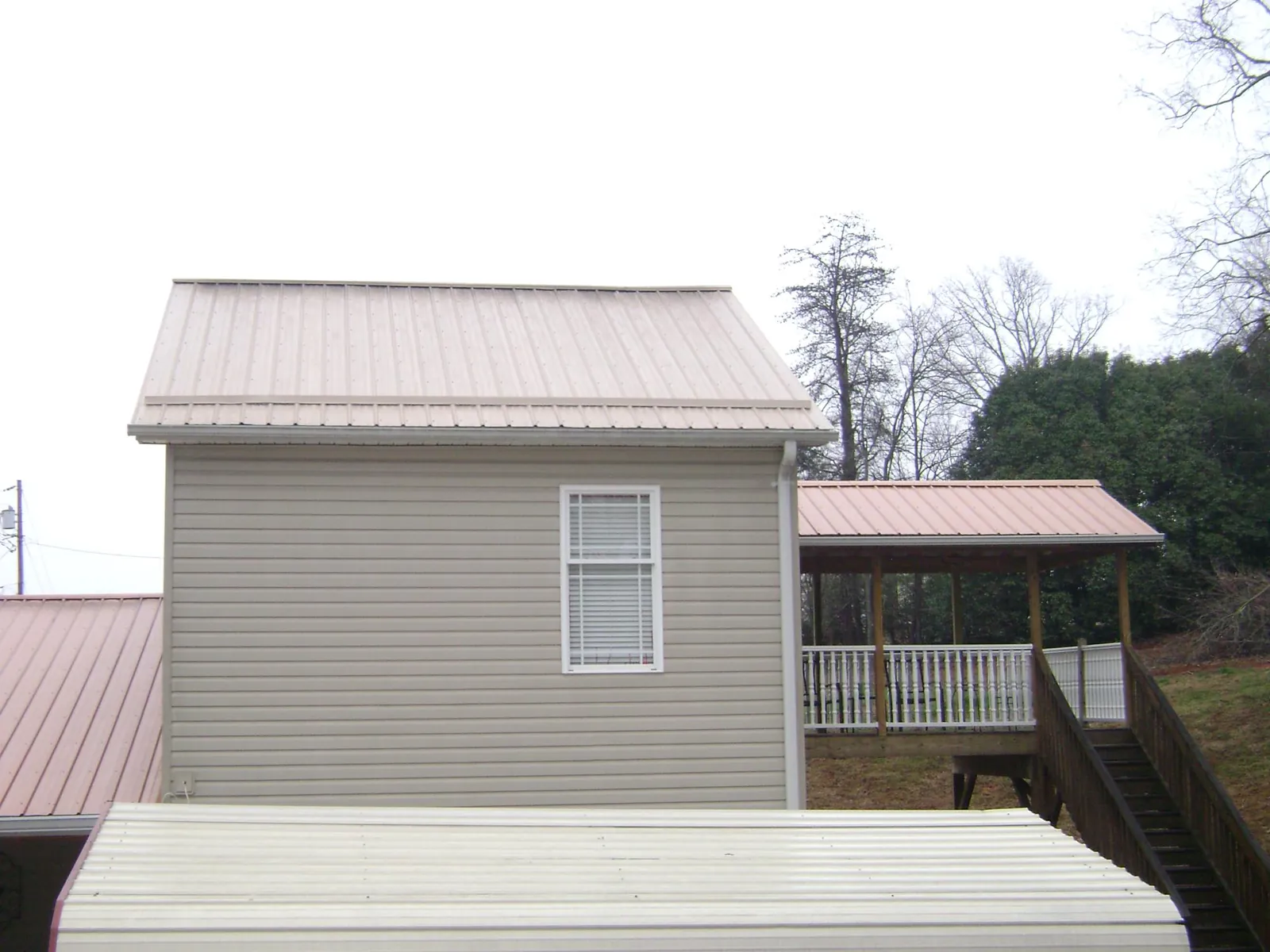Tan metal roofs on a two story addition and attached porch, from a Roof Replacement job in Crab Orchard